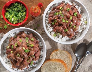 2 bowls of Red Beans and rice topped with green onions next to 2 pieces of whole white bread and a cup of chopped green onions