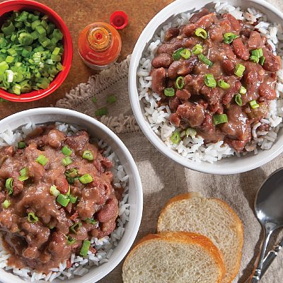 2 bowls of Red Beans and rice topped with green onions next to 2 pieces of whole white bread and a cup of chopped green onions