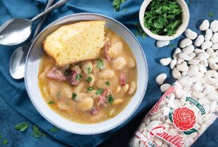 a bowl of Southern Large Limas and sausage with a side of corn bread on top next to a package of camellia brand large lima beans