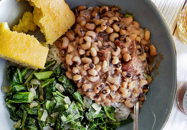 a plate of black eyed peas and rice with a side of corn bread and collard grens