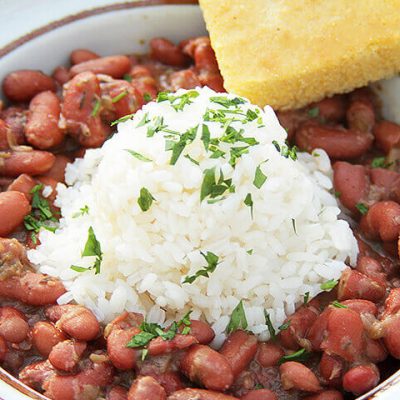 a close up of slow cooker red beans topped with rice with a side of corn bread