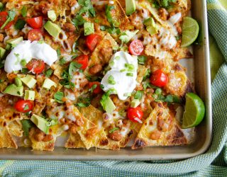 a pan of baked naked with beans, chilli, avacado, tomatoes, sour cream, and cut limes