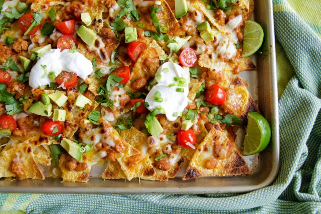 a pan of baked naked with beans, chilli, avacado, tomatoes, sour cream, and cut limes