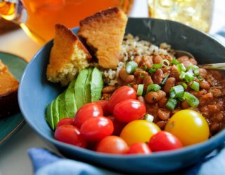 a bowl of chili rice and cornbread with a side of cherry tomatoes