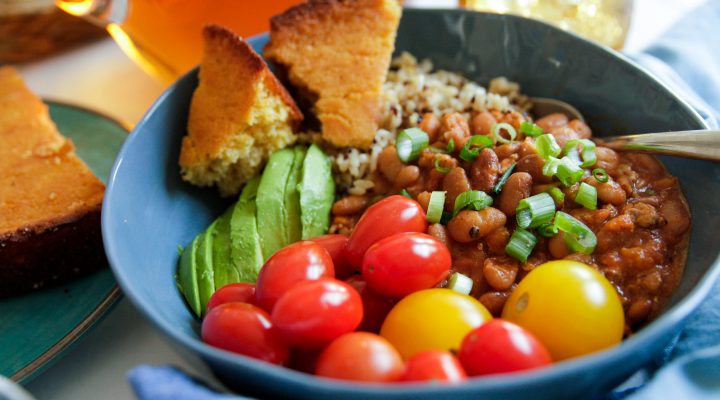 a bowl of chili rice and cornbread with a side of cherry tomatoes