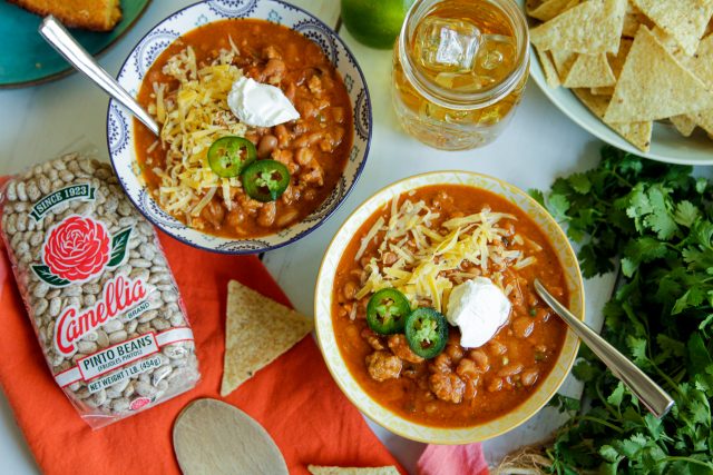 2 bowls of Instant Pot Pinto Chili next to a package of camellia branded pinto beans and tortilla chips