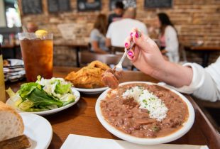 a person eating red beans and rice with a side of chicken and a bread with a small salad with a glass of sweet tea at mena's palace