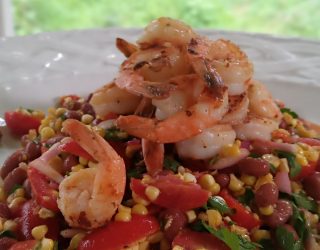 a close up of a plate of grilled corn, shrimp and pink bean salad