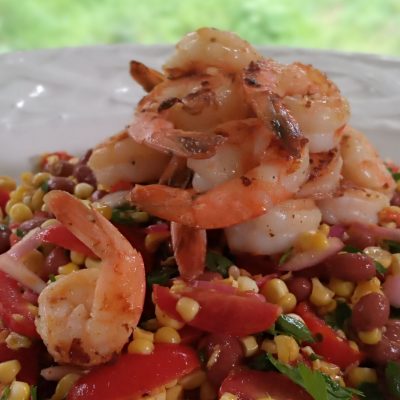 a close up of a plate of grilled corn, shrimp and pink bean salad