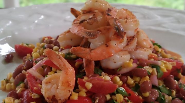 a close up of a plate of grilled corn, shrimp and pink bean salad