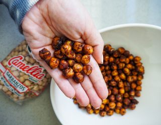 a hand holding a few texas honey chickpea garganzo beans in their hand while over the plate of texas honey chickpea garganzo beans next to a package of camellia brand garbanzo beans