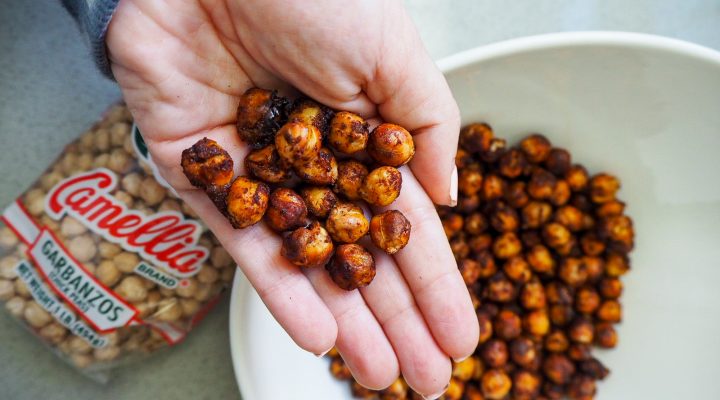 a hand holding a few texas honey chickpea garganzo beans in their hand while over the plate of texas honey chickpea garganzo beans next to a package of camellia brand garbanzo beans