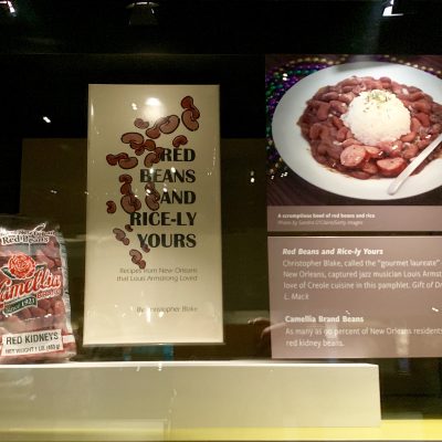 a display at the smithsonian showing a package of camellia brand red beans, some images and a picture of a plate of red beans and rice