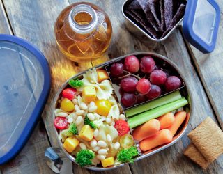 white beans and pasta with corn, broccoli and tomatoes ina lunch box with grapes and celery and carrots as a side