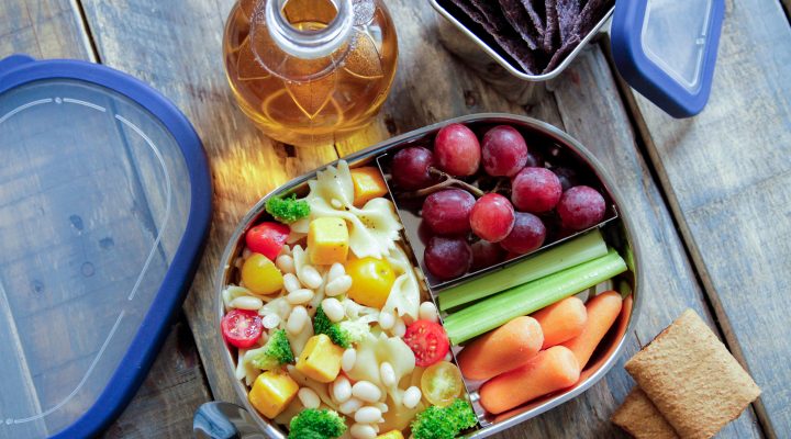 white beans and pasta with corn, broccoli and tomatoes ina lunch box with grapes and celery and carrots as a side