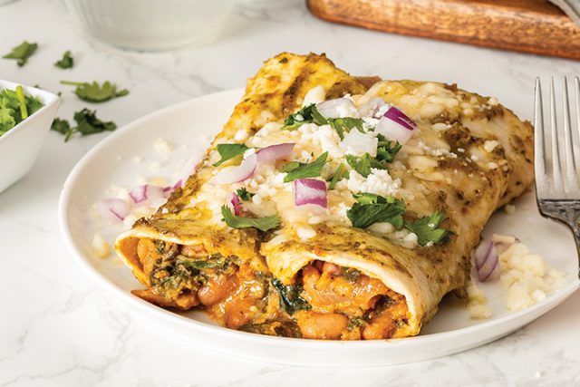 2 Tomatillo Sauce Enchiladas on a plate covered with purple onions, cillantro and a type of cheese