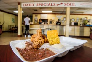 Hurst Restaurant red beans and rice plate lunch with 2 peices of chicken, corn bread and a side of mashed potatoes sitting at a table overlooking the order counter with customers