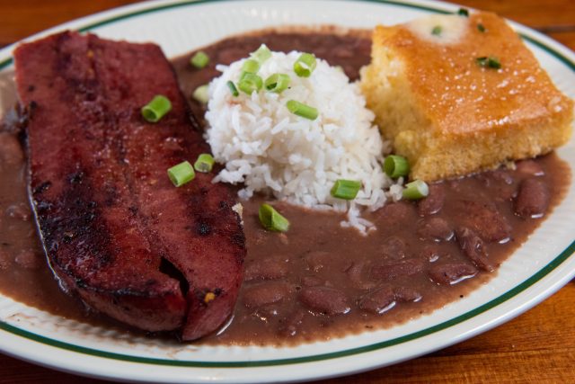 A plate of cooked red beans and rice, buttered cornbread, and grilled sausage.
