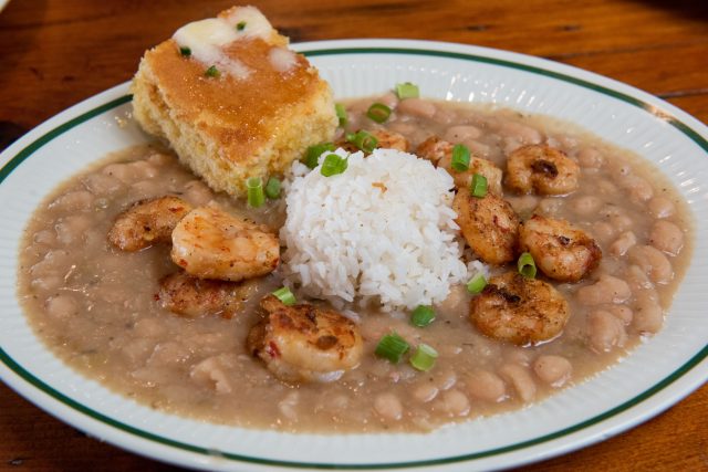 A plate of white beans, rice, buttered cornbread and sautéed shrimp on top of a table.