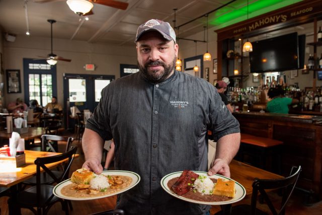 Chef of Mohony's holding a plate of cooked red beans and rice, and a plate of white beans and rice.
