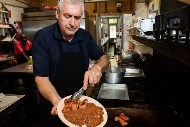 The owner of Leni's Restaurant holding a plate of red beans, rice and sausage