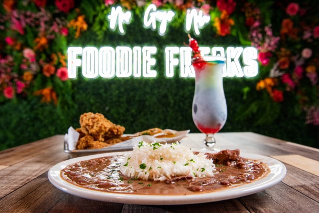 A plate of red beans, rice and friend chicken on a table, and a frozen daiquiri on a table. A sign that reads Foodie Freaks.
