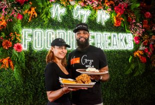 Employees holding plated red beans and rice with fried chicken in front of Nice Guys Nola Food Freaks sign