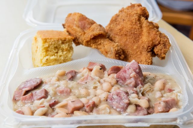 Plate of fried chicken, white beans and ham and a slice of cornbread.