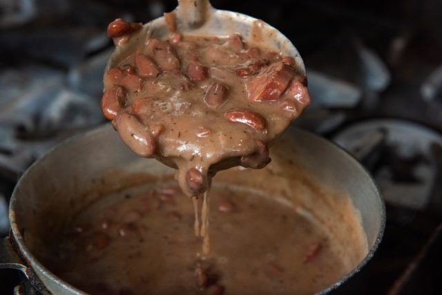 a cooking ladel full of red beans taking a spoon full out of the pot of red beans