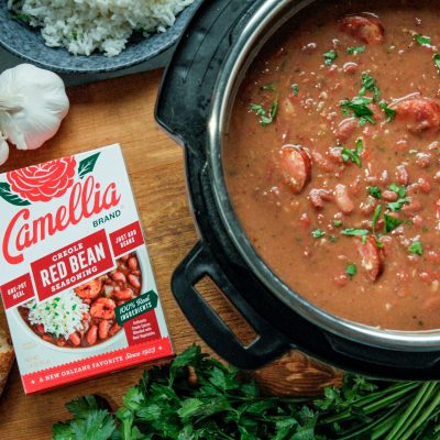 a top down view of a dutch oven full of red beans next to a box of camellia brand creole seasoning