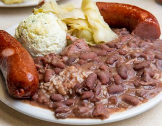 a close up of a plate of red beans and rice with a side of mashed potatoes, 2 sausage links, and some chips from mother's restaurant