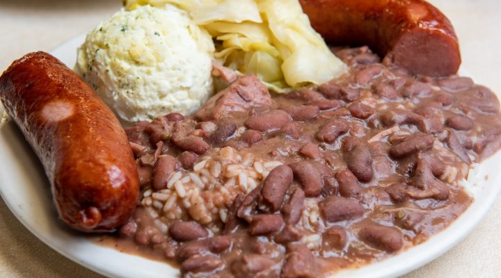 a close up of a plate of red beans and rice with a side of mashed potatoes, 2 sausage links, and some chips from mother's restaurant