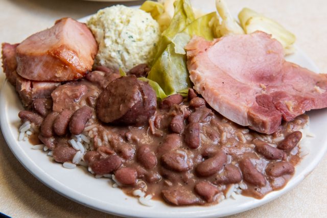A plate of red beans and rice with ham, potato salad and cabbage