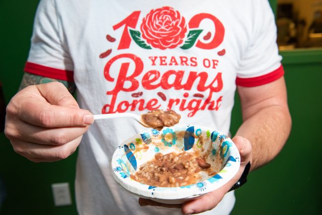 A man wearing a tshirt that reads 100 years of beans done right. He is holding a bowl of redbeans and rice.