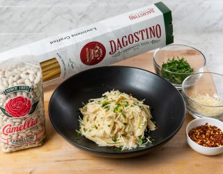 black bowl with cooked Creamy White Bean and Leek Fettuccine Alfredo surrounded by bag of beans and box of pasta and small bowls of other ingredients