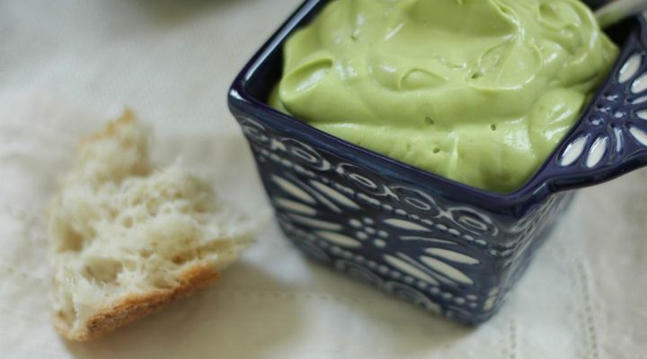 a close up of a dipping cup of avocado dressing and dip with a piece of bread