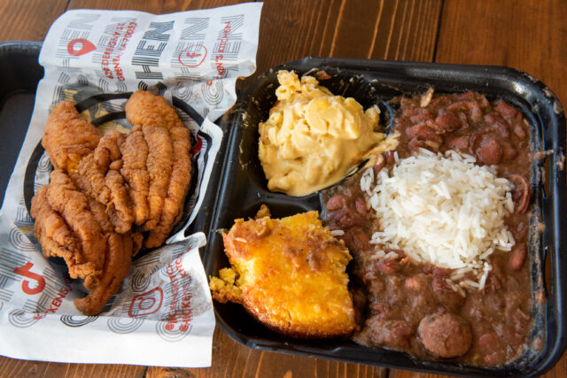 a top down view of a to go box full of red beans and rice with a side of corn bread, mac and cheese and fried chicken
