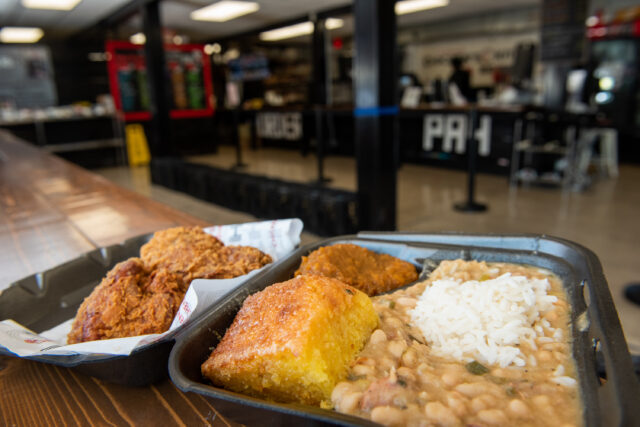 a to go box full of white beans and rice with a side of corn bread and fried chicken from chicken's kitchen
