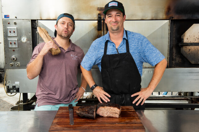 the owners of Blue Oak BBQ Restaurant standing behind a cooked piece of emat