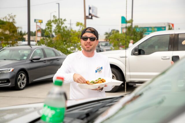 Devin Snow eating red beans outside of a restaurant with cars around him