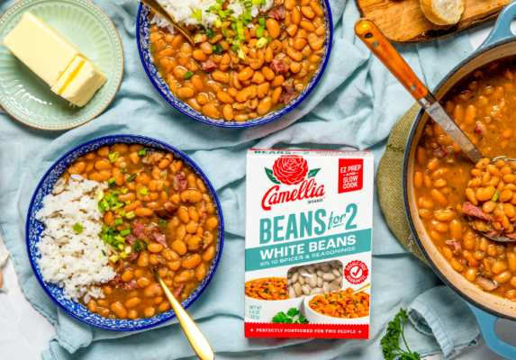 Two bowls of bean stew with rice, butter and bread on a blue table, plus a Camellia Beans for Two box in the center.