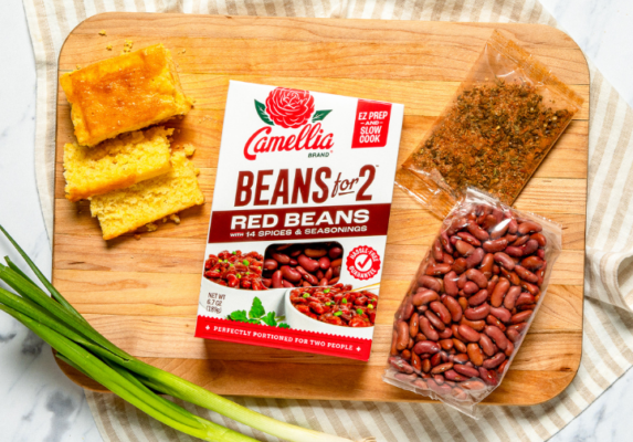 Box of Camellia Beans for Two Red Beans and 14 spices on a wooden cutting board, surrounded by cornbread, a seasoning packet, and a bag of red beans.