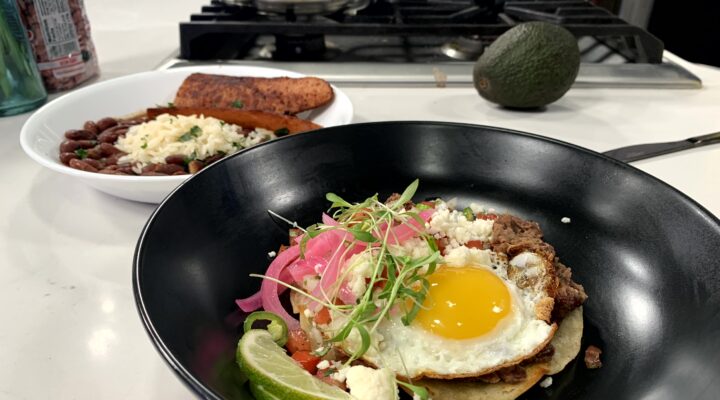 a close up of a dish of red bean huuvos rancheros with a side of red beans and rice with sausage