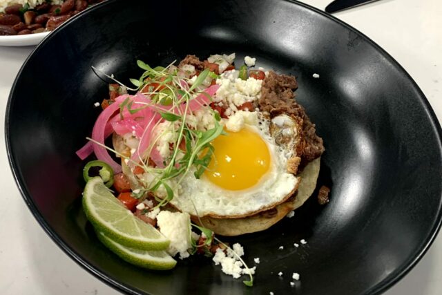 a close up of a dish of red bean huuvos rancheros wwith a side of red beans and rice with sausage