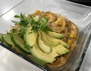 a close up of a dish of white bean chicken chili, topped with avocado slices