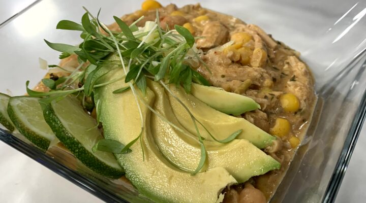 a close up of a dish of white bean chicken chili, topped with avocado slices
