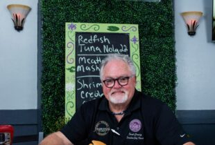 chef standing infront of sign at Katie's resturant posing with 2 plates of red beans and rice