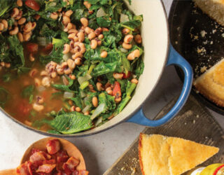 overhead image of large pot of cooked greens and blackeyed peas surrounded by cornbread on the table