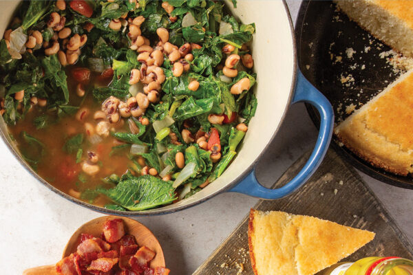 overhead image of large pot of cooked greens and blackeyed peas surrounded by cornbread on the table