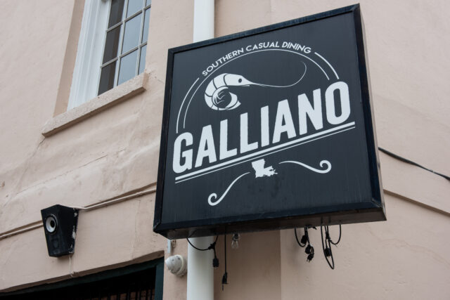 Exterior, hanging, square, black, restaurant sign, with white font reading “Galliano” in all caps, and “Southern Casual Dining” in smaller text above restaurant name, with a drawing of a prawn in between